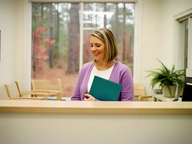 A clinic office manager holding a folder behind a reception counter.